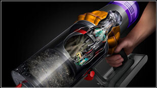 Zdjęcie przedstawia rękę trzymającą odkurzacz z widocznym przezroczystym pojemnikiem na kurz, w którym znajdują się zanieczyszczenia. Widać także elementy mechaniczne i kolorowe detale obudowy.