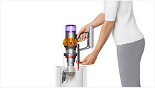 Osoba opróżnia pojemnik odkurzacza do kosza na śmieci. Odkurzacz ma przezroczysty pojemnik i kolorowe elementy w górnej części.