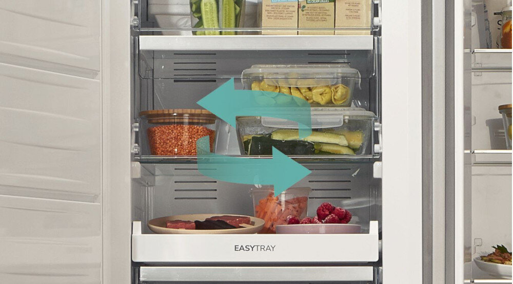 Wnętrze zamrażarki z kilkoma półkami, na których znajdują się różne produkty spożywcze w pojemnikach. Na dolnej szufladzie widoczny jest napis \'EASYTRAY\'.