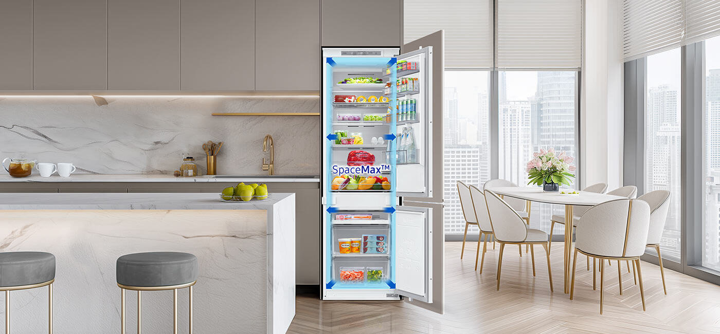 większa przestrzeń użytkowa przy standardowych wymiarach zewnętrznych w lodówce do zabudowy brb80f26acs0eo W nowoczesnej kuchni znajduje się otwarta lodówka z napisem \'SpaceMax™\', wypełniona różnorodnymi produktami spożywczymi. W tle widoczny jest stół z krzesłami oraz duże okna z widokiem na miasto.