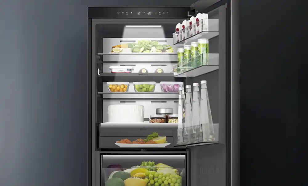 Wnętrze lodówki z kilkoma półkami, na których znajdują się różne produkty spożywcze, takie jak owoce, warzywa, napoje i nabiał. Drzwi lodówki mają dodatkowe półki z napojami i kartonami.