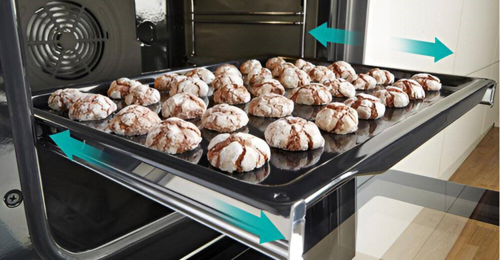 Blacha z ciasteczkami umieszczona w piekarniku, z widocznymi strzałkami wskazującymi kierunek ruchu. W tle widać wnętrze piekarnika z wentylatorem.