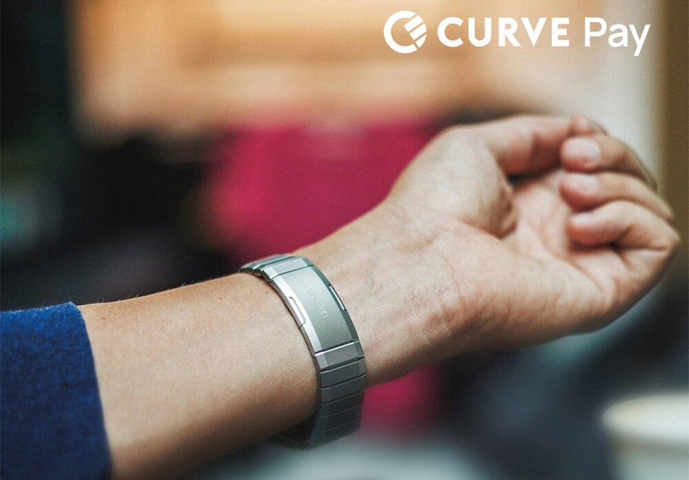 Na zdjęciu widoczna jest ręka z metalową bransoletką, na której znajduje się napis \'CURVE\'. W prawym górnym rogu widnieje logo i tekst \'CURVE Pay\'.