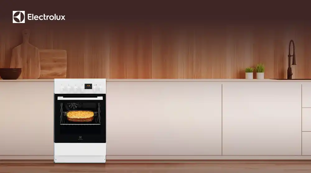 Na obrazie widoczna jest biała kuchnia z piekarnikiem, w którym znajduje się zapiekanka. W lewym górnym rogu znajduje się logo Electrolux.