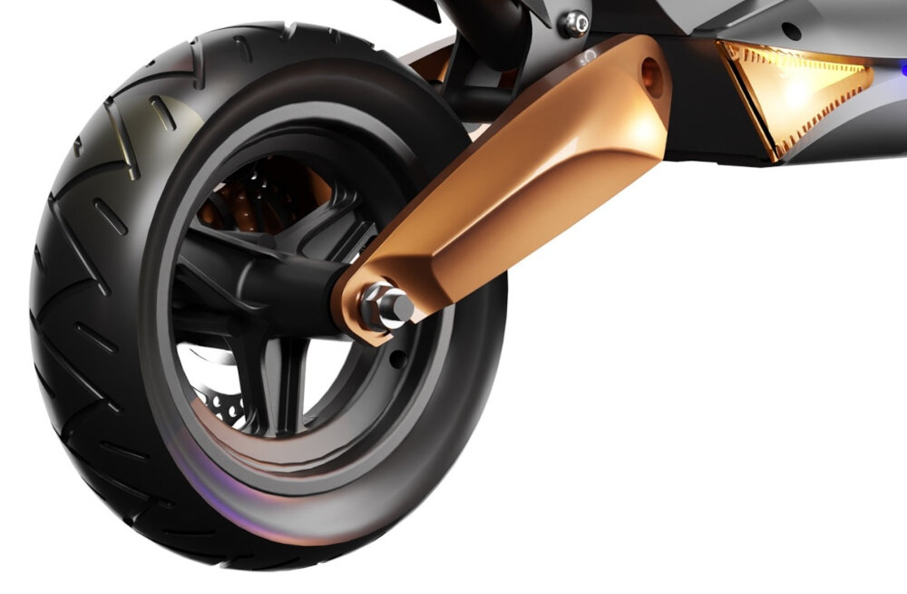 Zbliżenie na koło hulajnogi elektrycznej z widocznym amortyzatorem w kolorze miedzianym. Opona jest czarna z wyraźnym bieżnikiem.