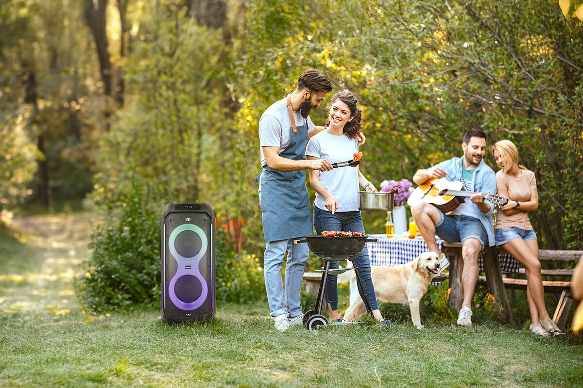 Power Audio MANTA SPK0805B140 PALLAS - Dźwięk dopasowany do Ciebie, urządzenie stojące na trawie, osoby robią sobie grilla