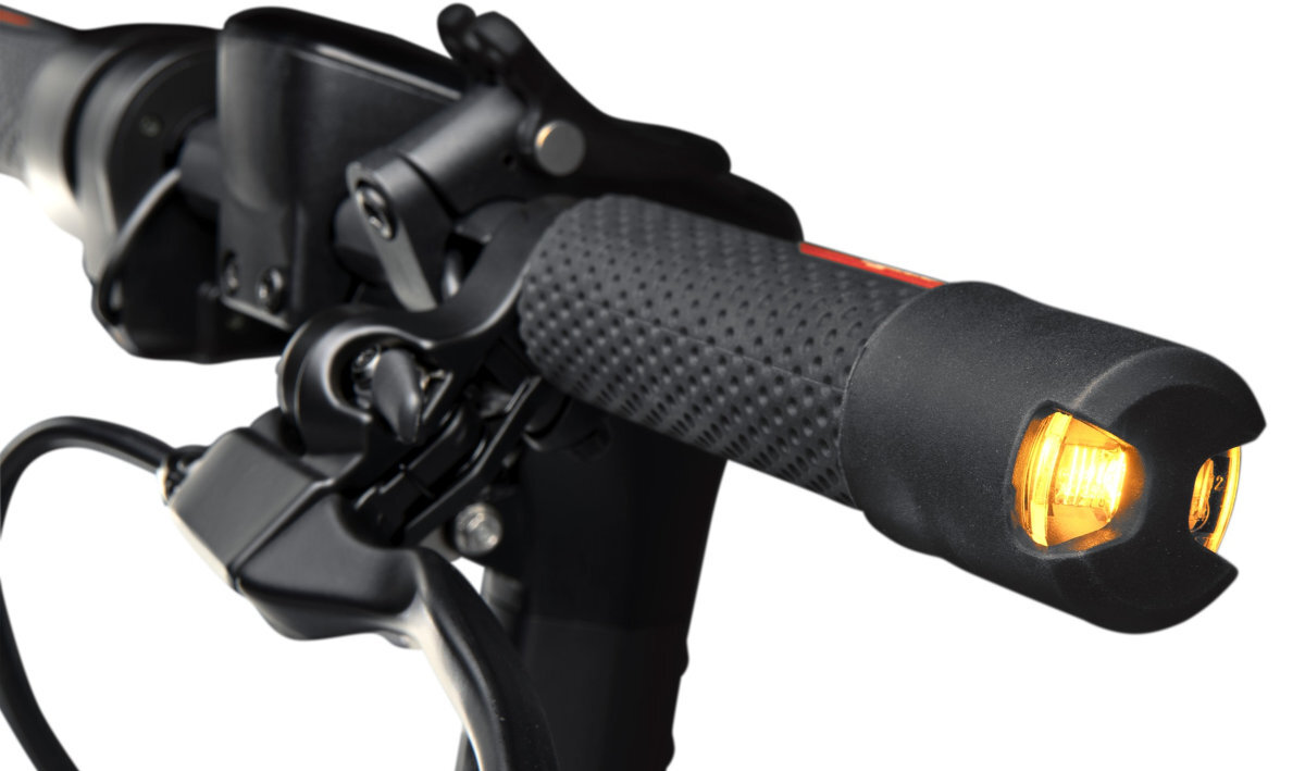 Zbliżenie na kierownicę hulajnogi elektrycznej z widocznym uchwytem i włączonym pomarańczowym światłem. Uchwyt jest czarny z teksturowaną powierzchnią.