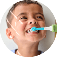 Dziecko uśmiecha się podczas używania szczoteczki sonicznej z niebieską końcówką i zieloną rączką.