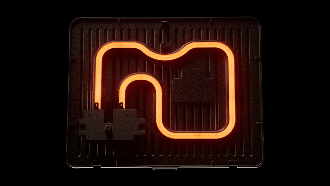 Obraz przedstawia element grzewczy w kształcie litery \'M\' na czarnej płycie grillowej. Element jest podświetlony na pomarańczowo, co sugeruje jego aktywność.