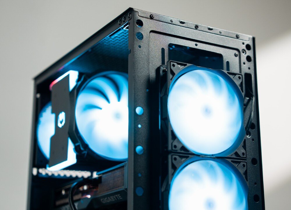 Obraz przedstawia fragment obudowy komputerowej z trzema podświetlanymi wentylatorami. Wewnątrz widoczna jest karta graficzna z napisem \'GIGABYTE\'.
