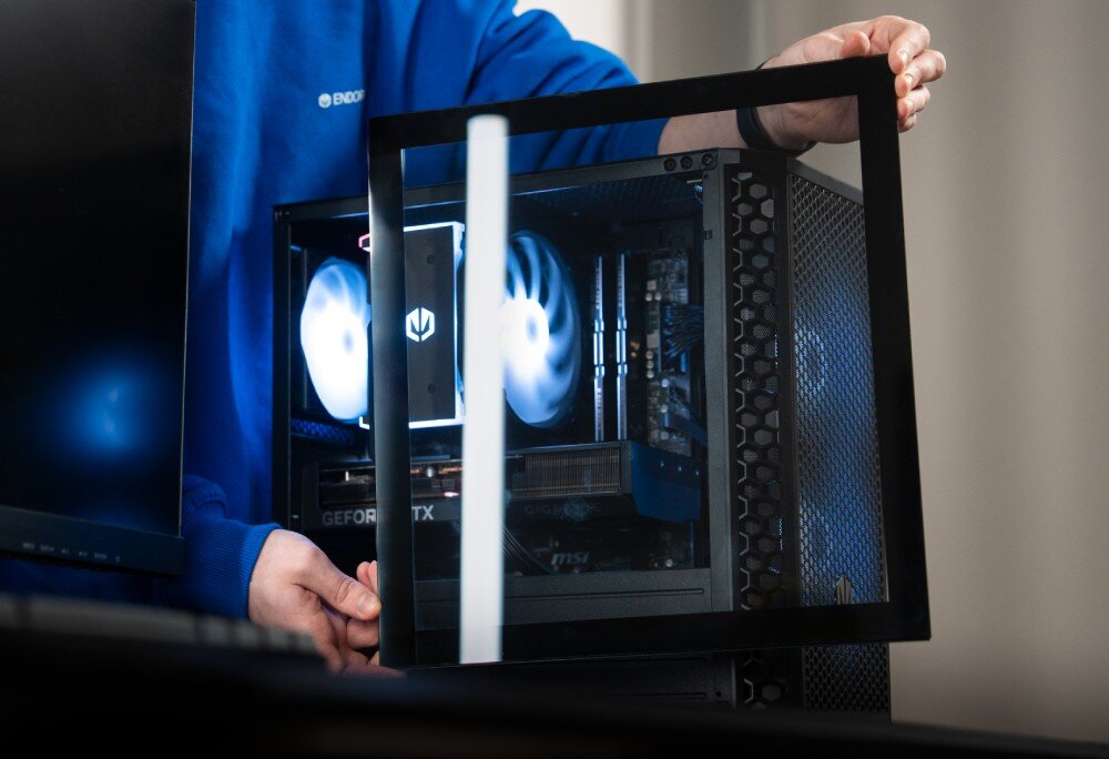 Osoba trzyma panel boczny obudowy komputera, ukazując wnętrze z podświetlonymi wentylatorami i komponentami. Na bluzie widoczny jest napis \'ENDORFY\'.