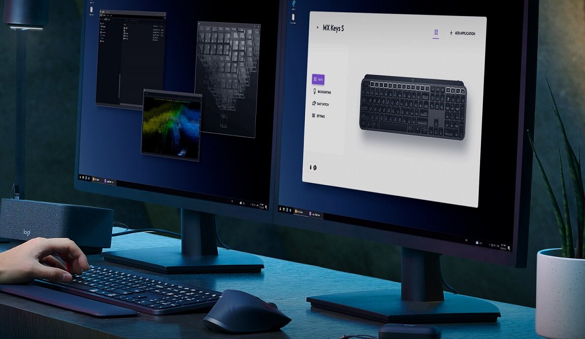 Na biurku znajdują się dwa monitory, klawiatura i myszka. Na jednym z monitorów wyświetlony jest obraz klawiatury z napisem \'MX Keys S\'.