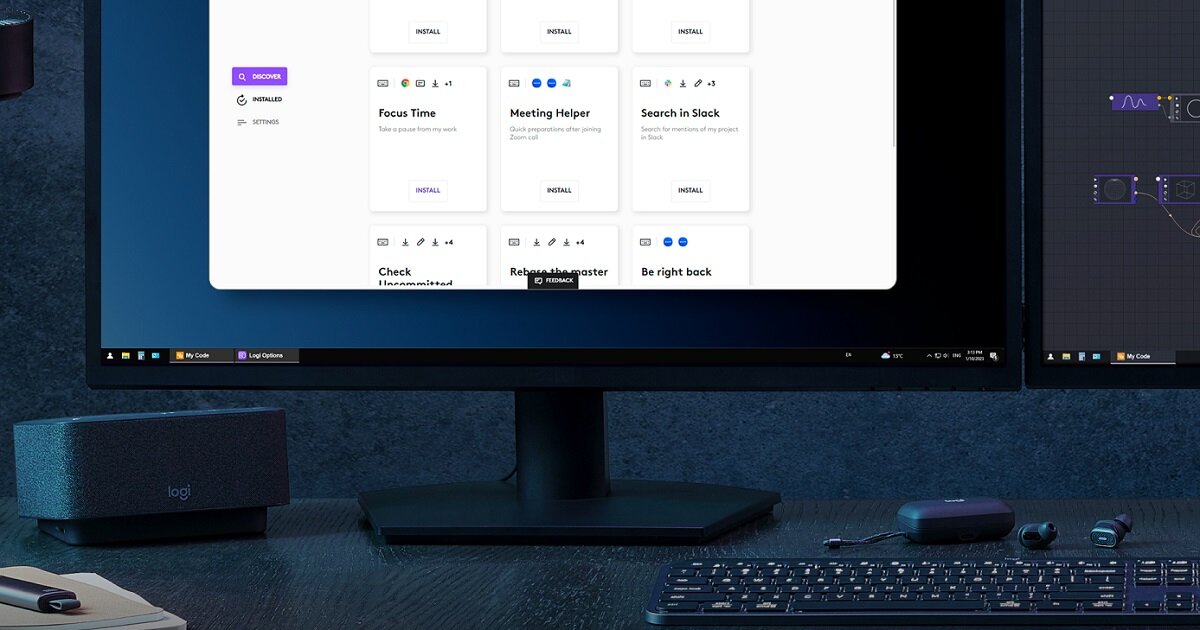 Na biurku znajduje się monitor z wyświetlonym interfejsem aplikacji oraz klawiatura i mysz. Obok monitora widoczny jest głośnik z logo \'logi\'.
