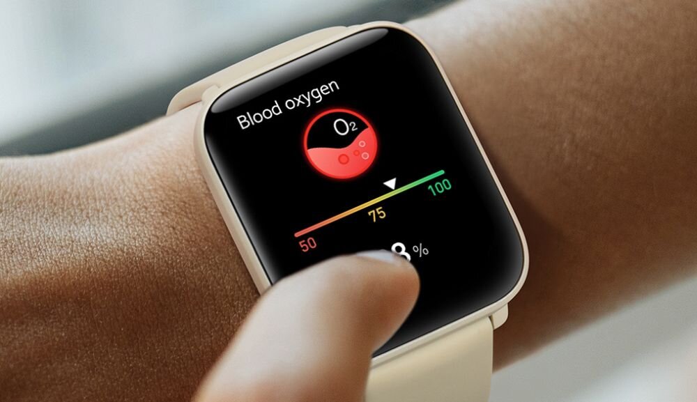 Na zdjęciu widać smartwatch z białym paskiem, na którym wyświetlany jest ekran z napisem \'Blood oxygen\' oraz wskaźnikiem poziomu tlenu we krwi wynoszącym 98%.