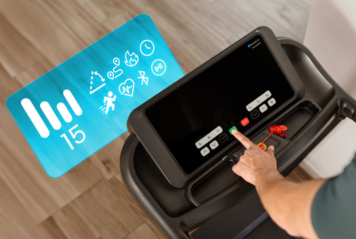 Osoba naciska przycisk na panelu sterowania bieżni elektrycznej z dużym ekranem. Obok ekranu widoczna jest niebieska grafika z ikonami i liczbą 15.