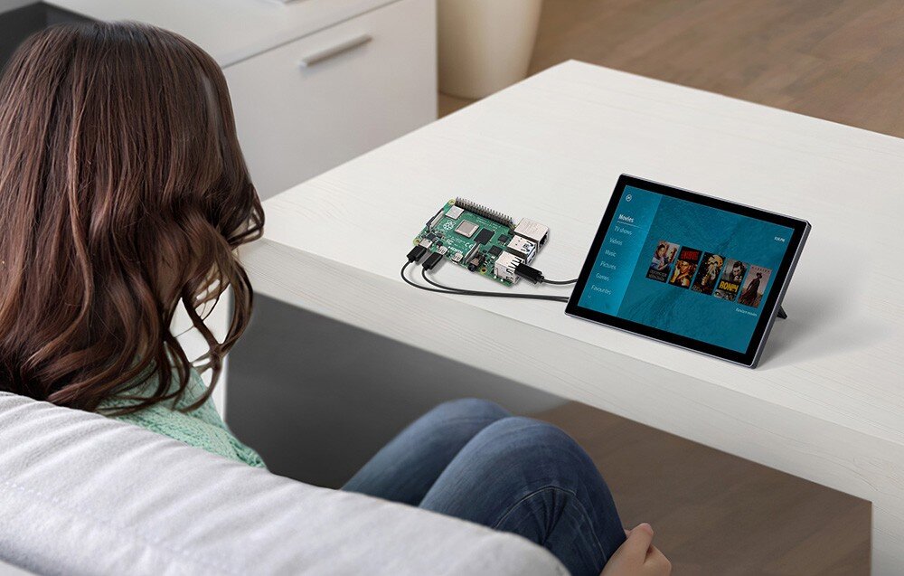 Monitor UPERFECT UPI B7 Osoba siedząca przy stoliku ogląda ekran podłączony do płytki komputerowej, na wyświetlaczu menu z filmami, kompatybilność, montaż, systemy