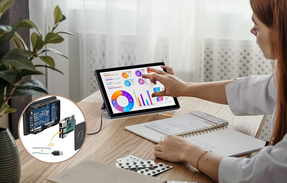Monitor UPERFECT UPI B7 Kobieta siedząca przy biurku korzysta z ekranu dotykowego wyświetlającego kolorowe wykresy, obok zeszyt i ołówek, na ekranie w rogu pokazane schematy podłączeń urządzeń, porty, podłączenie