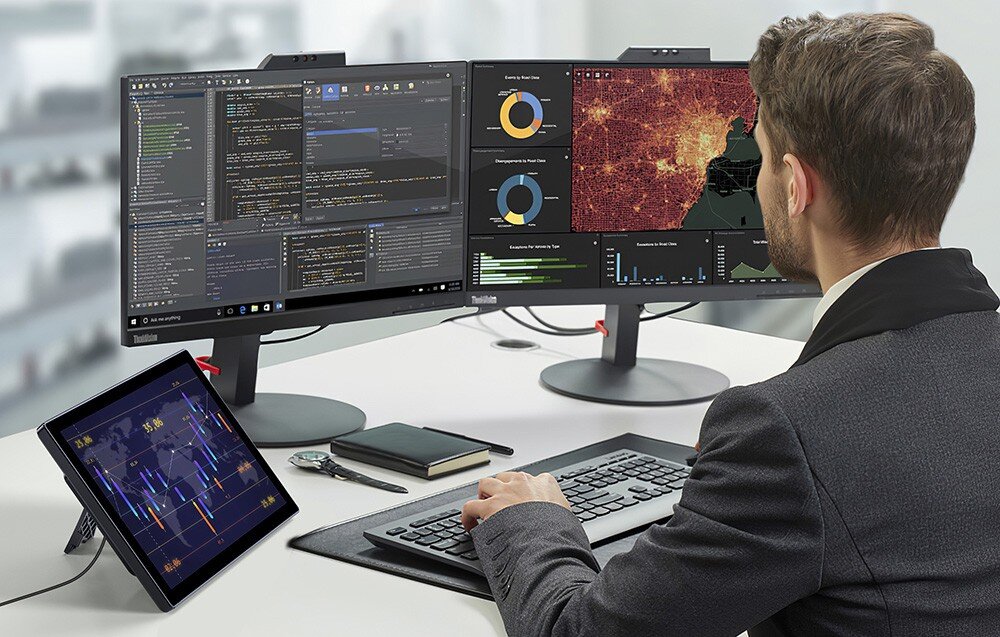 Monitor UPERFECT UPI B7 Mężczyzna w garniturze pracuje przy dwóch dużych monitorach z wykresami i mapami, obok ustawiony dodatkowy ekran pokazujący dane giełdowe, stojak, regulacja nachylenia, montaż VESA