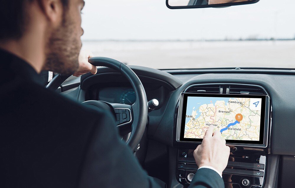 Monitor UPERFECT UPI B7 Mężczyzna prowadzący samochód dotyka ekranu zamontowanego w konsoli, na wyświetlaczu widoczna mapa z zaznaczoną trasą, wentylatory, chłodzenie