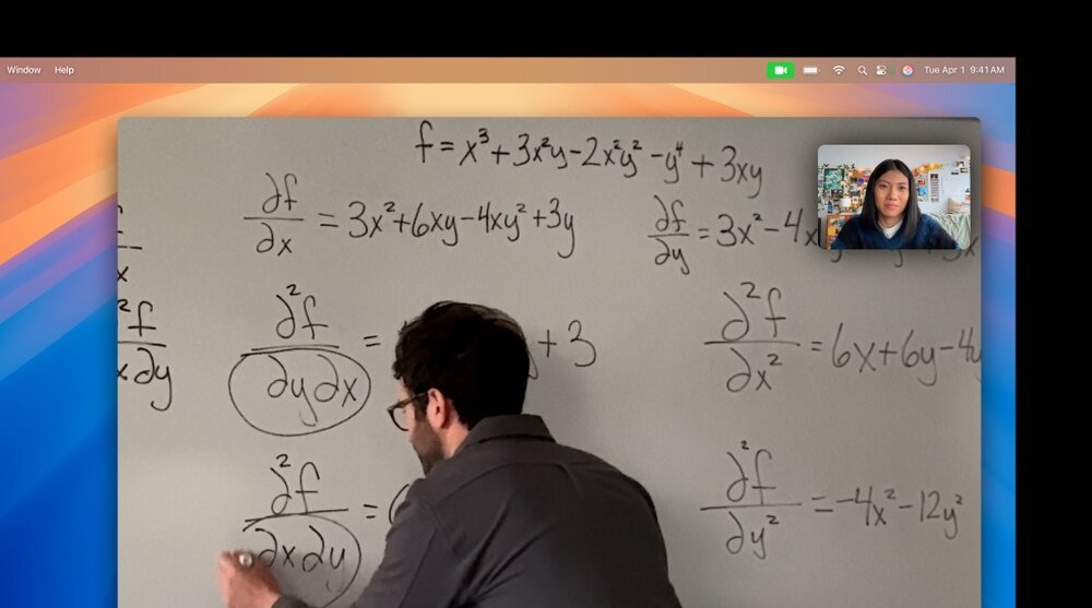 Osoba pisze równania matematyczne na tablicy, a w rogu ekranu widoczna jest inna osoba podczas wideorozmowy. Na tablicy znajdują się równania z pochodnymi cząstkowymi, takie jak df/dx = 3x^2 + 6xy - 4xy^2 + 3y.