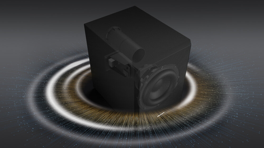 Obraz przedstawia czarny subwoofer z widocznym głośnikiem, otoczony efektami świetlnymi przypominającymi fale dźwiękowe. Tło jest ciemne, co podkreśla wizualizację dźwięku.