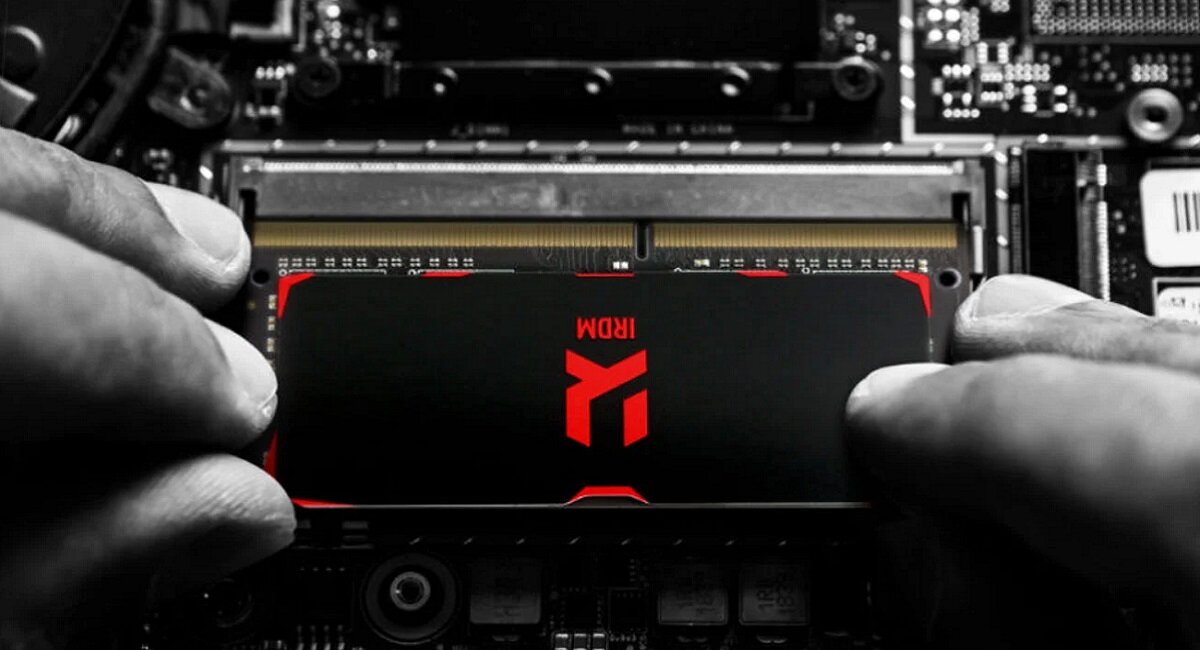 Osoba instaluje moduł pamięci RAM z widocznym logo \'IRDM\' na płycie głównej. Pamięć ma czarną obudowę z czerwonymi akcentami.