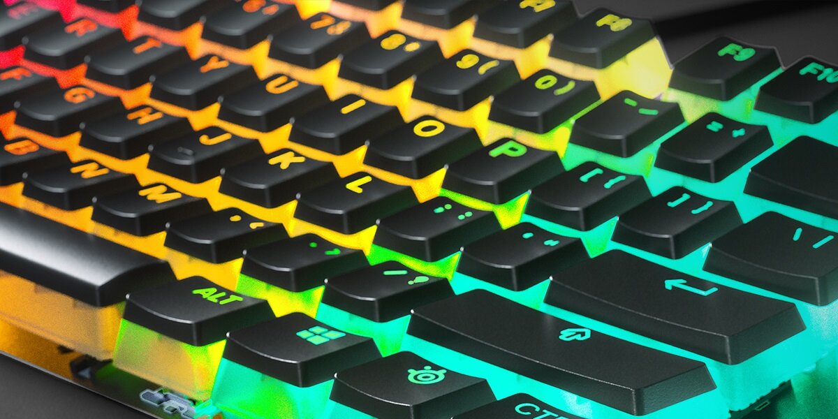 Zdjęcie przedstawia klawiaturę z czarnymi klawiszami, które są podświetlone w różnych kolorach, takich jak żółty, pomarańczowy i zielony. Widoczne są klawisze z oznaczeniami liter i symboli, w tym \'ALT\', \'CTRL\' oraz logo producenta.