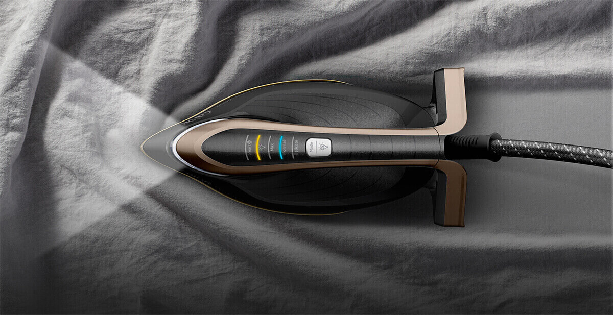 Generator pary z oświetleniem LED przesuwa się po tkaninie, emitując światło na materiał. Urządzenie ma ciemną obudowę z widocznymi przyciskami i kolorowymi wskaźnikami.