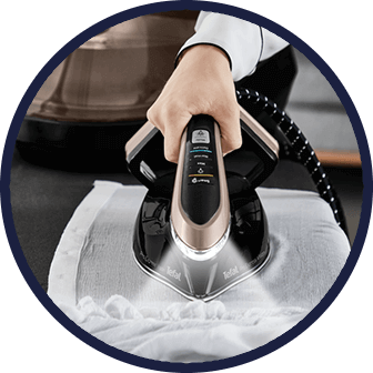 Osoba prasuje białą tkaninę za pomocą generatora pary z oświetleniem LED. Na urządzeniu widoczne jest logo \'Tefal\'.