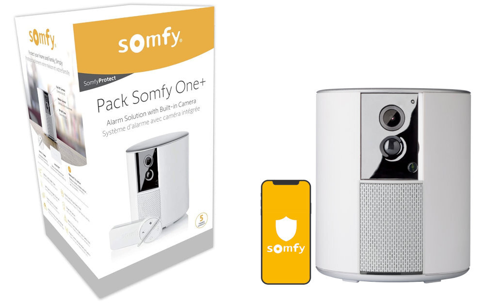 Na obrazie znajduje się opakowanie systemu alarmowego Somfy One+ oraz sam system alarmowy w postaci białego urządzenia z kamerą. Obok urządzenia widoczny jest smartfon z logo Somfy na ekranie.