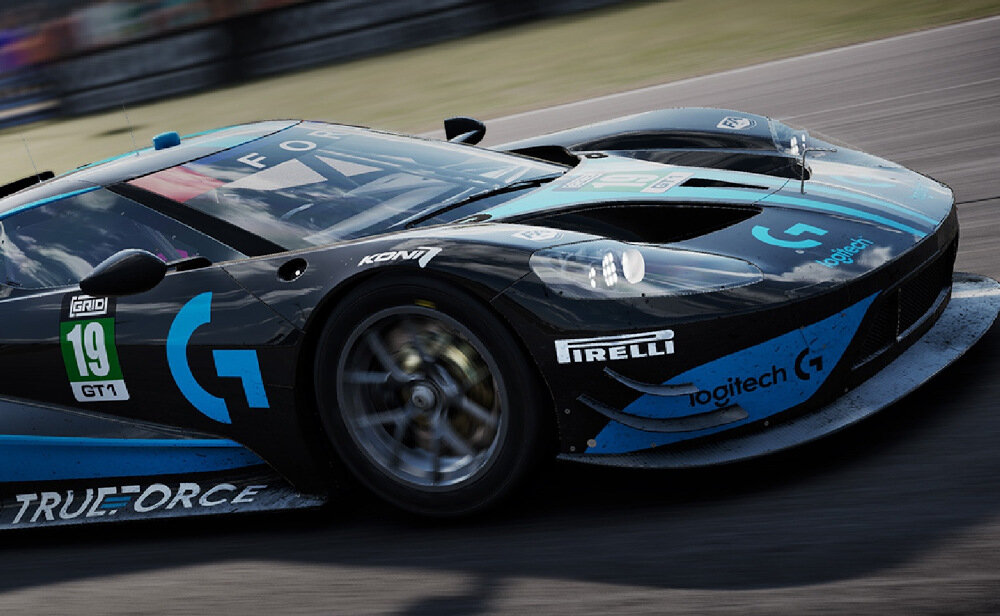 Na obrazie widoczny jest wyścigowy samochód z numerem 19, ozdobiony logotypami \'Pirelli\', \'Logitech G\', \'TRUEFORCE\' oraz innymi. Samochód ma czarno-niebieskie barwy i znajduje się na torze wyścigowym.