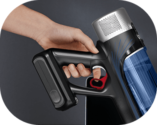 Osoba trzyma odkurzacz z niebieskim pojemnikiem i czarnym uchwytem, naciskając czerwony przycisk. W tle widoczna jest ciemna powierzchnia.