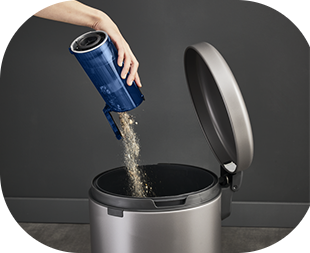 Osoba opróżnia pojemnik na kurz do otwartego kosza na śmieci. Pojemnik jest niebieski, a kosz ma metaliczny kolor.