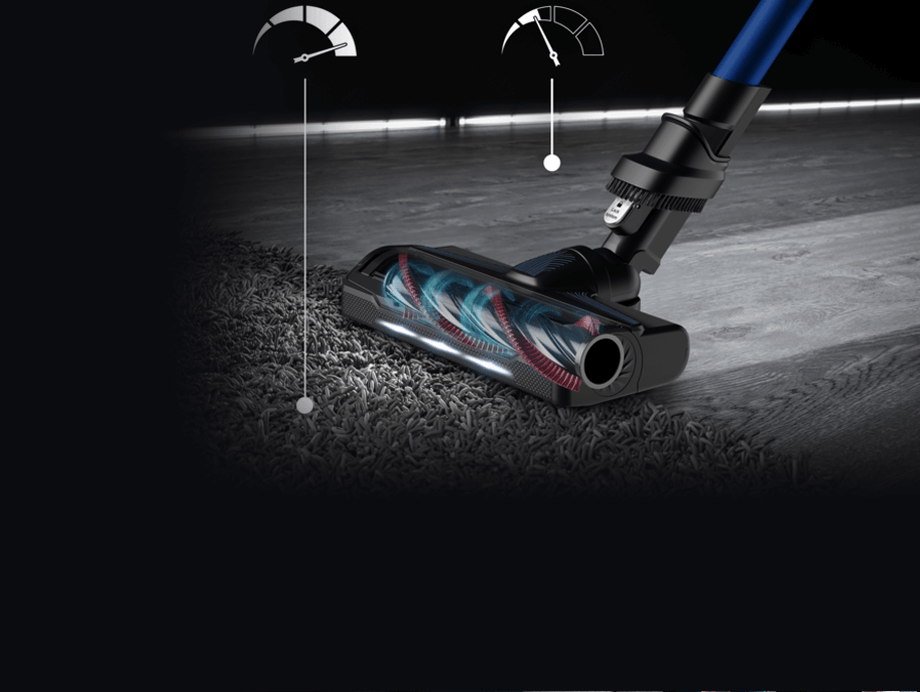 Odkurzacz z niebieską rurą i szczotką z podświetleniem, częściowo na dywanie, częściowo na podłodze. W tle widoczne są dwa wskaźniki w kształcie zegarów.