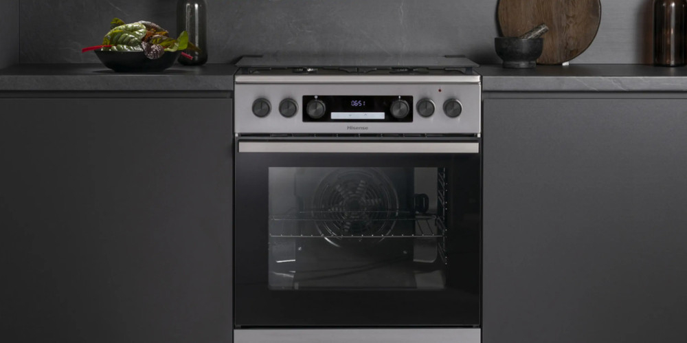 Nowoczesna kuchnia wolnostojąca z piekarnikiem i płytą grzewczą, w kolorze stalowym. Na wyświetlaczu widoczny jest czas 05:51, a na blacie znajdują się akcesoria kuchenne.