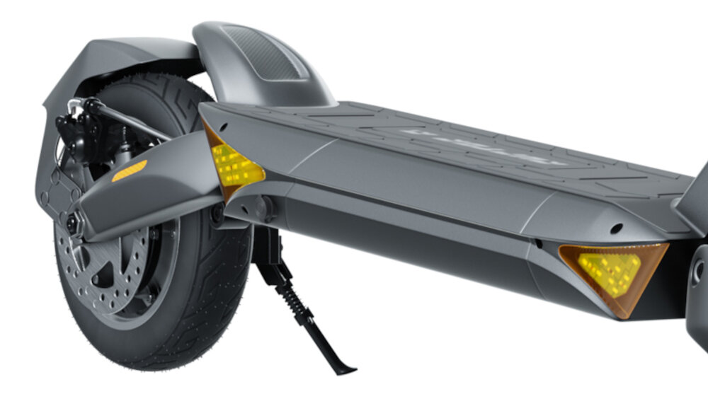 Czarna hulajnoga elektryczna z widocznym tylnym kołem, amortyzatorem i podnóżkiem. Na obudowie znajdują się żółte odblaski.