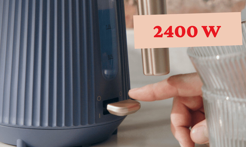 Na zdjęciu widać niebieski czajnik z pionowymi żłobieniami oraz napis \'2400 W\'. Obok czajnika znajduje się ręka naciskająca przycisk.