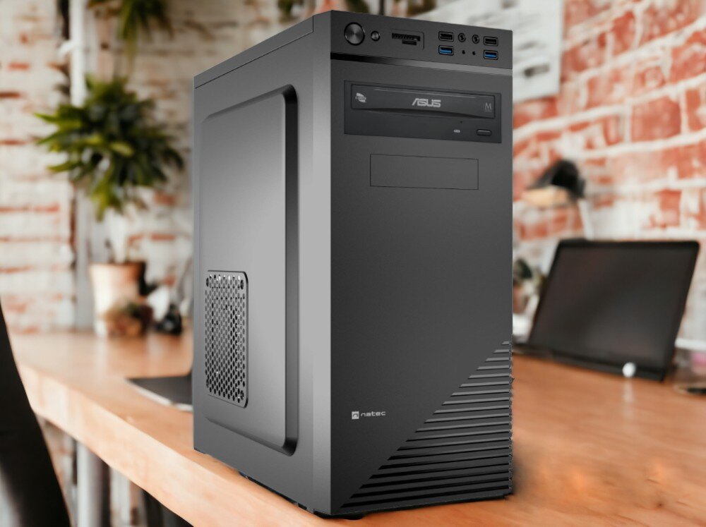 Na drewnianym biurku stoi czarna obudowa komputera z widocznym logo \'natec\' i napędem optycznym \'ASUS\'. W tle znajduje się rozmyty widok biura z laptopem i roślinami.