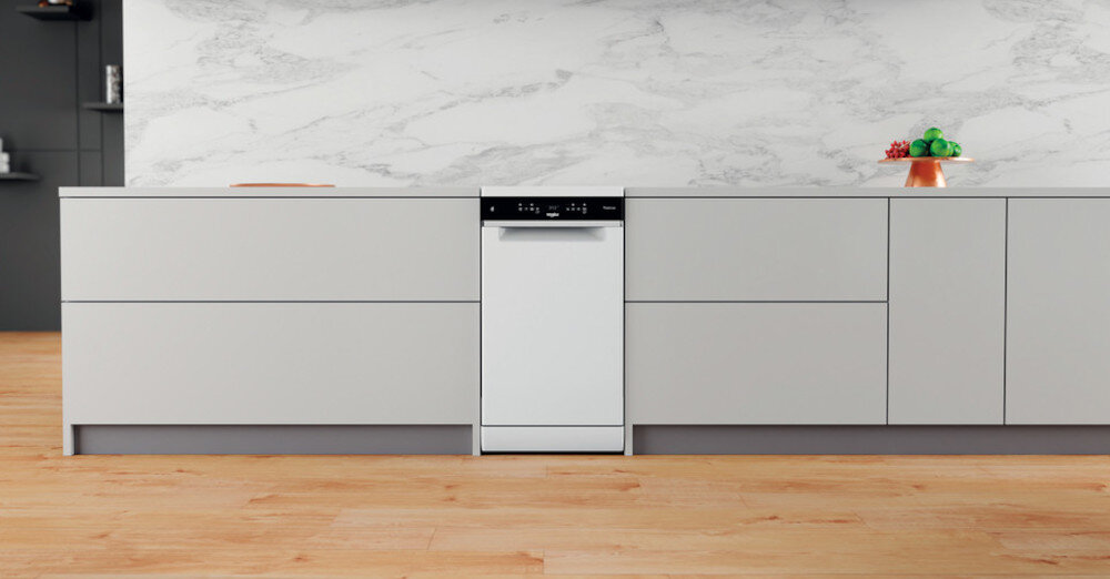 Biała zmywarka wbudowana w nowoczesną kuchenną zabudowę z szarymi frontami. Na blacie znajduje się patera z owocami oraz deska do krojenia.