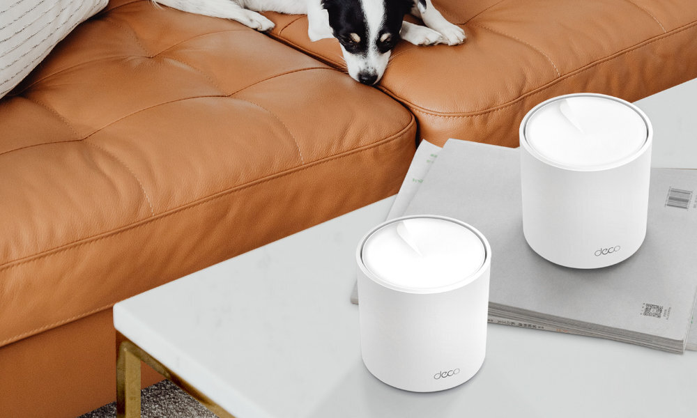 Na białym stole znajdują się dwa białe urządzenia z napisem \'deco\'. W tle widać brązową kanapę, na której leży pies.
