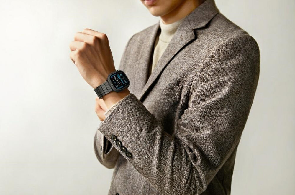 Osoba w eleganckiej marynarce prezentuje zegarek na nadgarstku. Zegarek ma ciemny pasek i wyświetlacz z widocznymi ikonami.