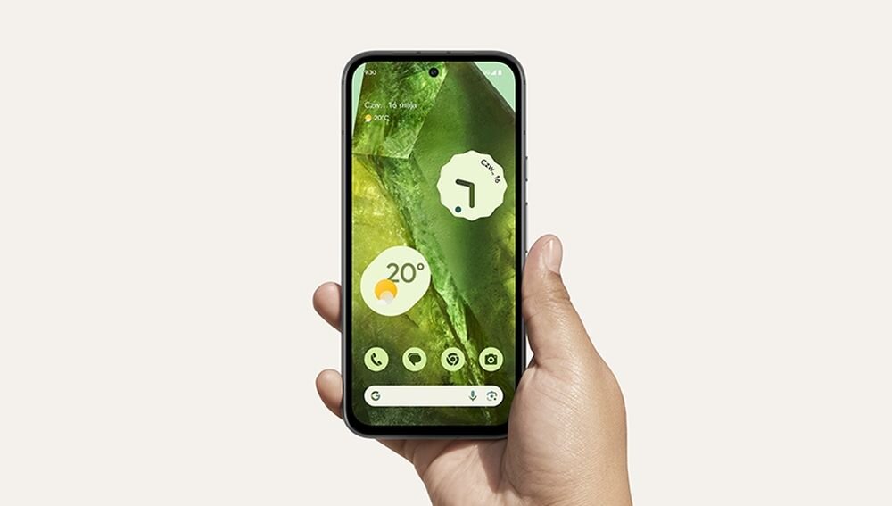 Osoba trzyma smartfon z wyświetlaczem pokazującym zielony motyw tapety oraz ikony aplikacji. Na ekranie widoczna jest temperatura 20° i data 16 sierpnia.