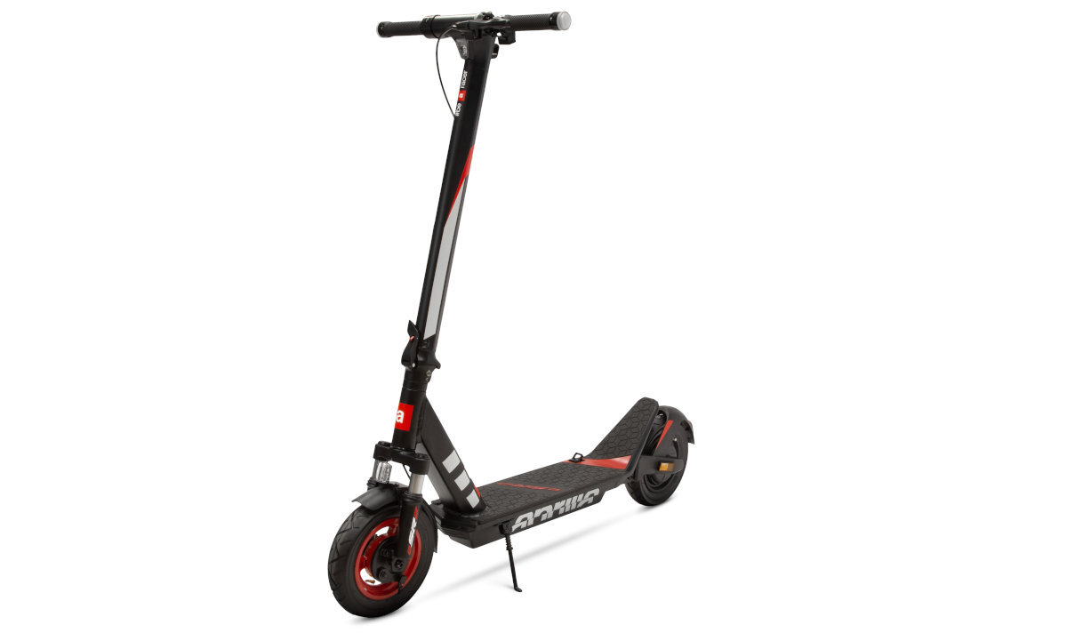 Czarno-czerwona hulajnoga elektryczna z dużymi kołami i prostą kierownicą. Na podeście widoczny jest napis \'APRILIA\'.