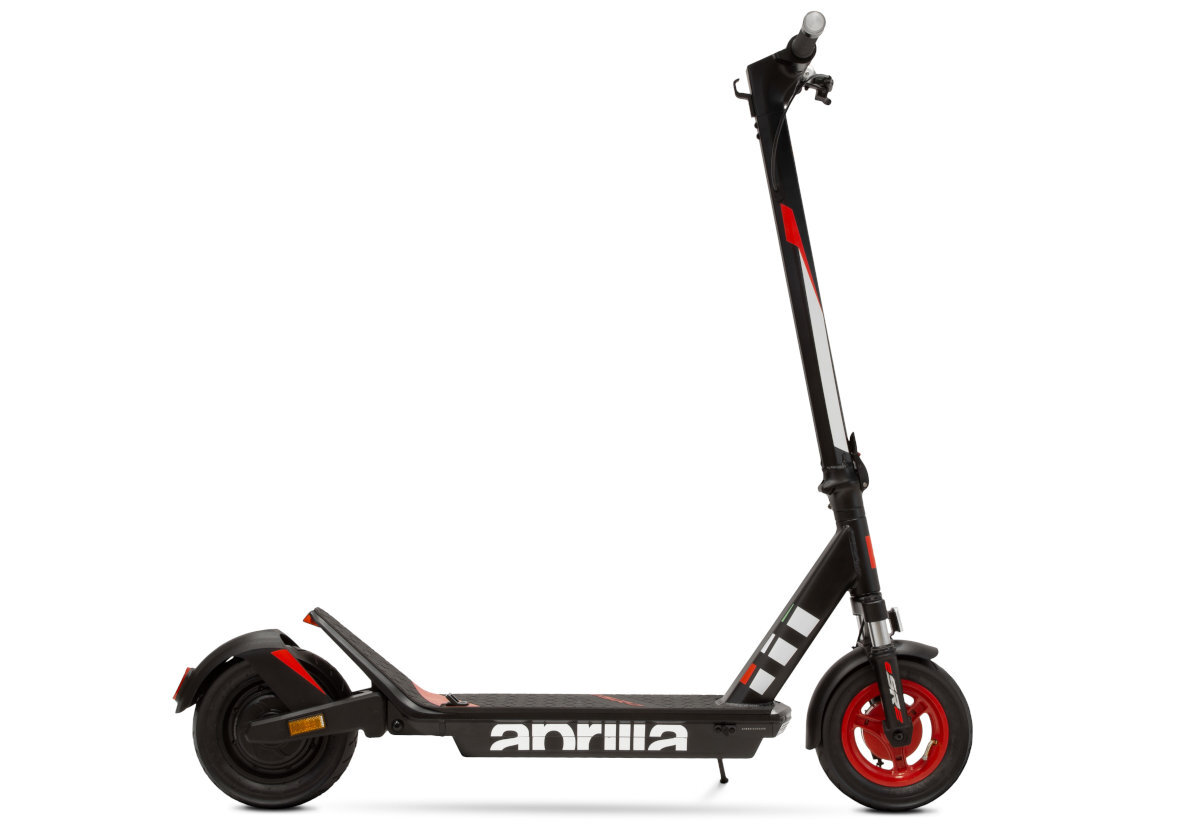 Czarno-czerwona hulajnoga elektryczna z widocznym logo \'aprilia\' na podeście. Posiada czerwone koła i czarne amortyzatory.