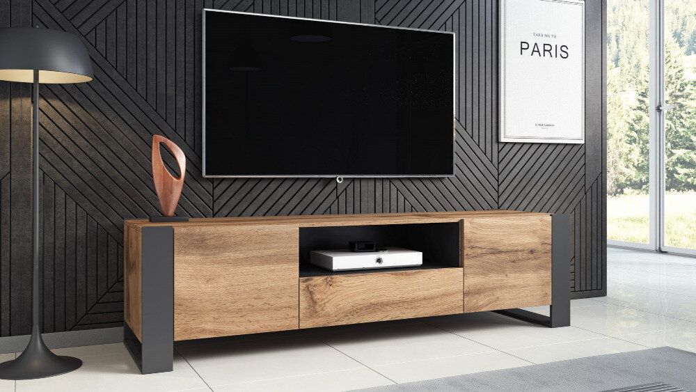 Szafka RTV w kolorze dąb wotan z antracytowymi elementami stoi na tle ciemnej, wzorzystej ściany. Na ścianie wisi duży telewizor, a obok znajduje się plakat z napisem \'PARIS\'.