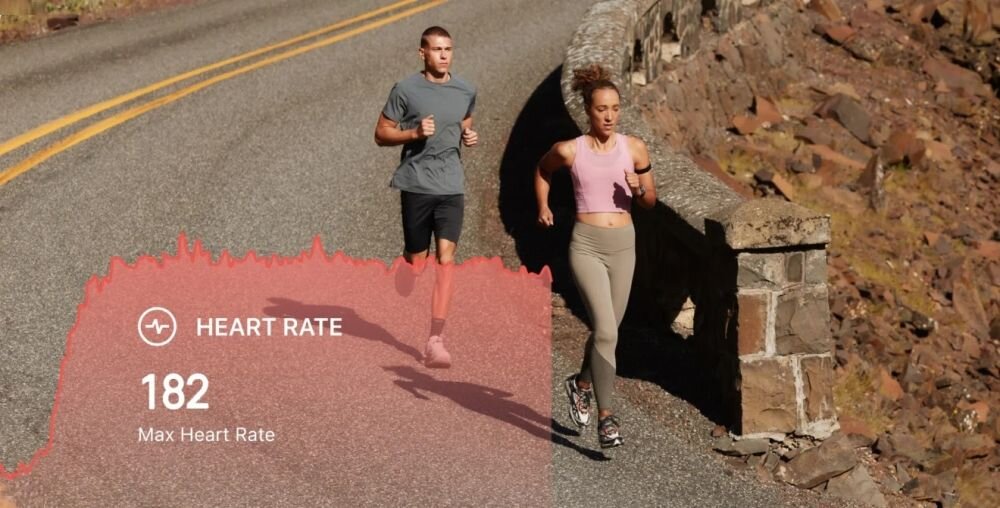 Dwie osoby biegną po asfaltowej drodze obok kamiennego muru. Na obrazie widoczny jest tekst: \'HEART RATE 182 Max Heart Rate\'.