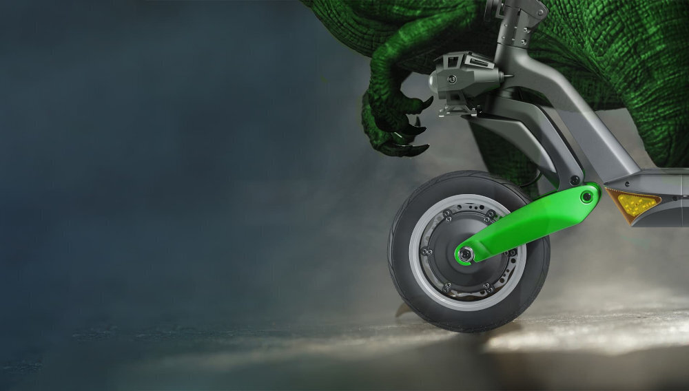 Obraz przedstawia fragment hulajnogi elektrycznej z widocznym kołem i zielonym elementem zawieszenia. W tle znajduje się zielony element przypominający łapę dinozaura.