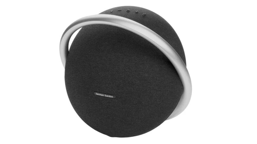 Czarny głośnik mobilny o okrągłym kształcie z metalowym uchwytem. Na powierzchni widoczne jest logo \'harman/kardon\'.