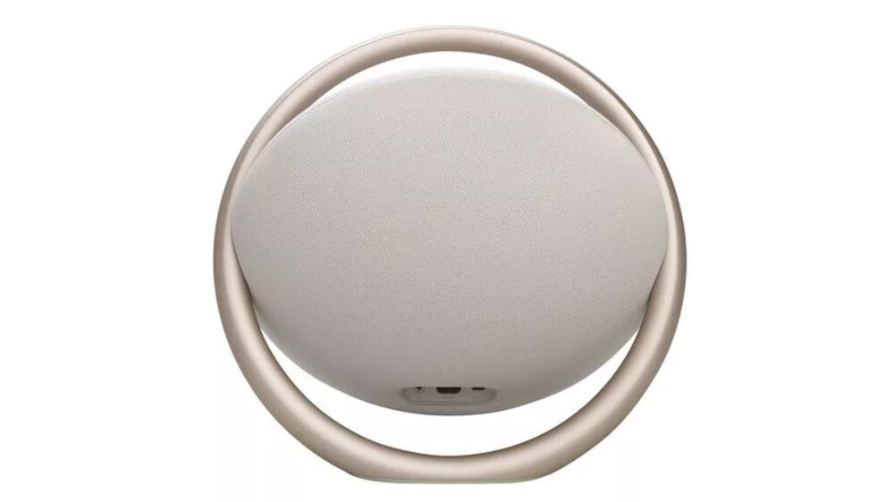 Na obrazie widoczny jest okrągły głośnik z uchwytem, w kolorze jasnoszarym. Głośnik ma minimalistyczny design z centralnie umieszczonym logo producenta.