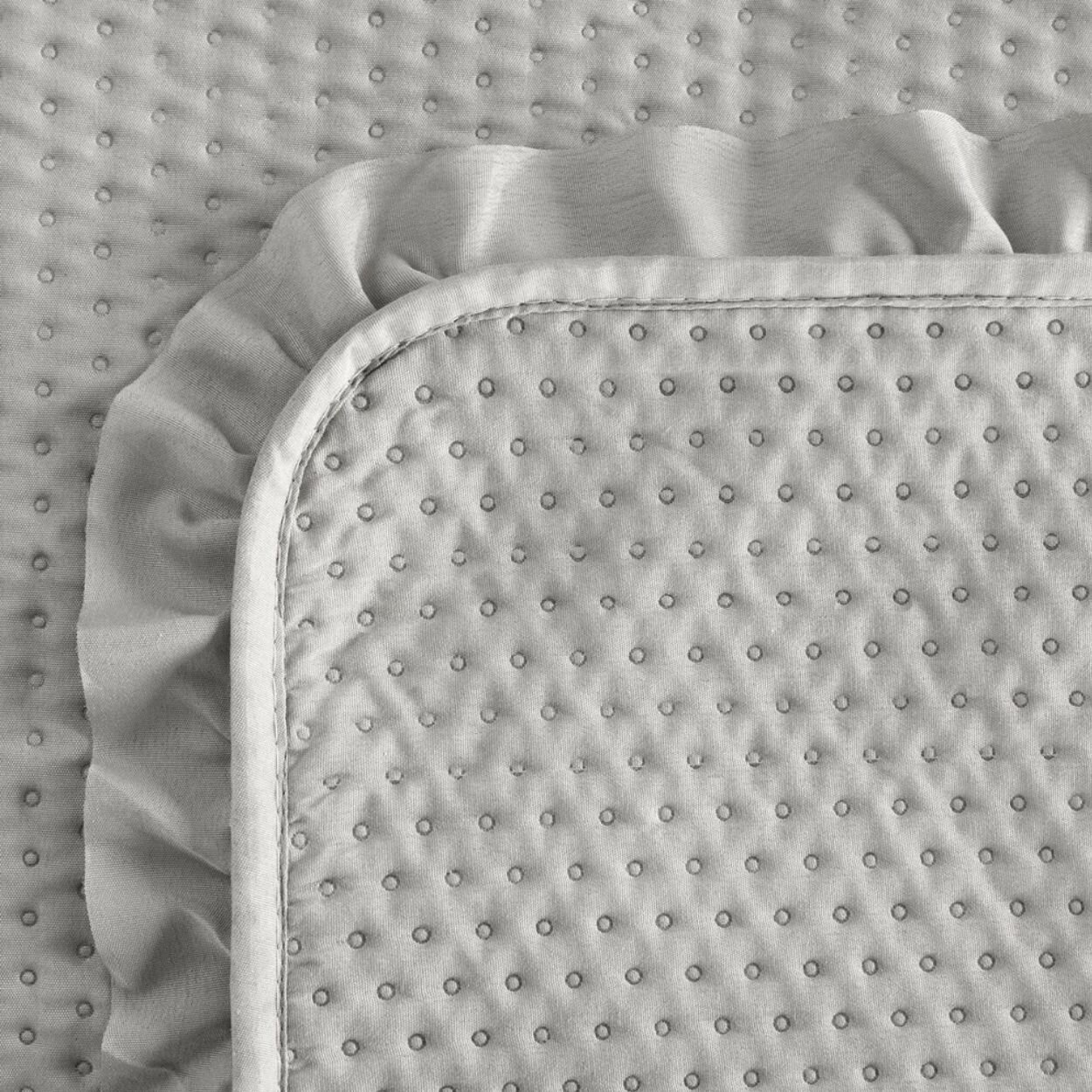Srebrna narzuta na łóżko z falbanką, pokryta regularnym wzorem małych kropek. Materiał ma delikatną teksturę i falbanki na krawędziach.